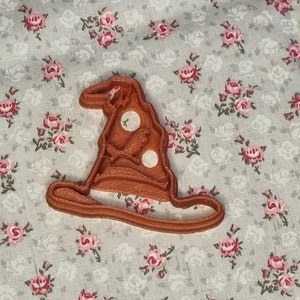 Könnte beinhalten: Ein brauner Plastik-Ausstecher in Form eines Zaubererhutes mit einer spitzen Spitze und einem breiten Rand. Der Hut hat drei weiße Kreise auf der Oberseite.