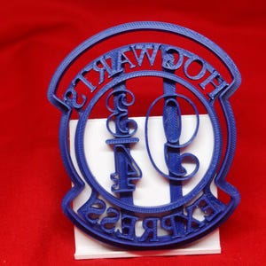 Könnte beinhalten: Ein blauer Plastik-Ausstecher in Form des Hogwarts Express-Logos. Das Logo zeigt die Worte "Hogwarts Express" und die Zahl "9 3/4" in einem Kreis.