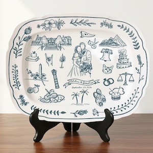 May include: A white ceramic serving platter with a scalloped edge and a blue floral border. The platter features a hand-drawn design with wedding-themed illustrations, including a couple, cake, and rings. Text reads "Catalina & Jarallan, September 25, 2026."