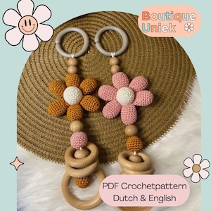 Op de afbeelding: Twee handgemaakte gehaakte bloem baby speelgoed. Eén bloem is mosterdgeel, de andere roze, beide met witte centra. Elk speelgoed heeft houten ringen en kralen. De tekst "Boutique Uniek" en "PDF Crochetpattern Dutch & English" zijn zichtbaar.