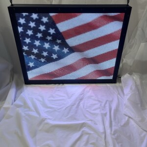May include: A black framed LED sign displaying the American flag. The flag is red, white, and blue with white stars on a blue field.