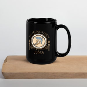 Puede incluir: Taza de cerámica negra con un diseño dorado que presenta un casco tachado y el texto "The People's Front of Judea".