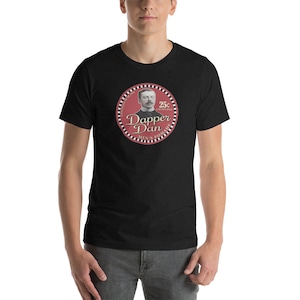 May include: Black t-shirt with a red circle graphic featuring a man in a suit and the text "Dapper Dan Men's Pomade 25c for six shaves only".