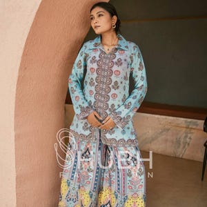May include: A light blue shirt and skirt co-ord set with a vibrant paisley design. The shirt features long sleeves and a collared neckline. The skirt is a maxi length with a wide hem. The outfit is a fashionable and coordinated ensemble.