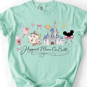 A mint green t-shirt with a Disney-themed design, including a castle, Belle, and various Disney characters. The text on the shirt reads "Happiest Mama On Earth".