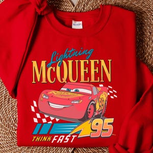 A red t-shirt with a Lightning McQueen graphic and the text "Think Fast" printed on it, along with a wicker placemat underneath.