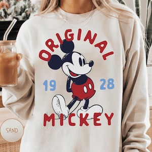 A person wearing a white sweatshirt with a graphic of Mickey Mouse and the text "ORIGINAL MICKEY" printed on it.