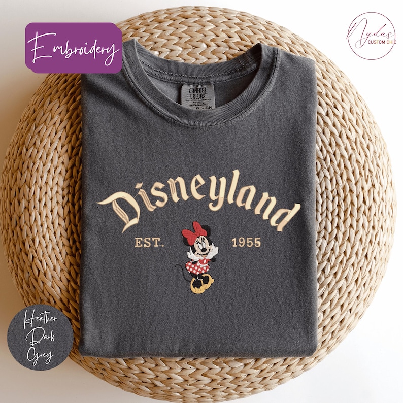 A gray t-shirt with the text "Disneyland EST. 1955" and a Minnie Mouse graphic, placed on a woven basket.