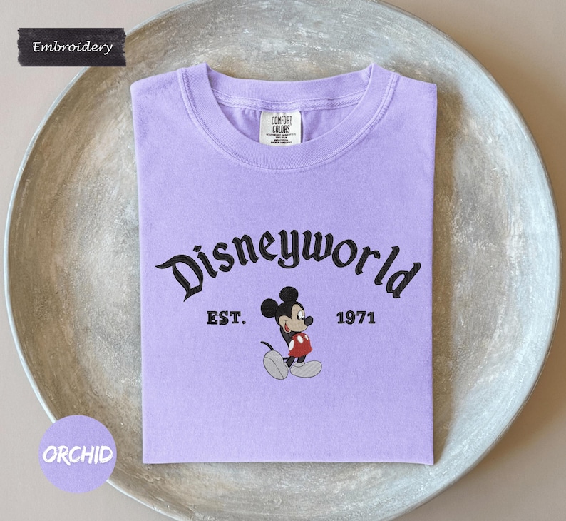 A purple t-shirt with the text "Disneyworld" and a Mickey Mouse graphic, along with the text "EST. 1971" printed on it.