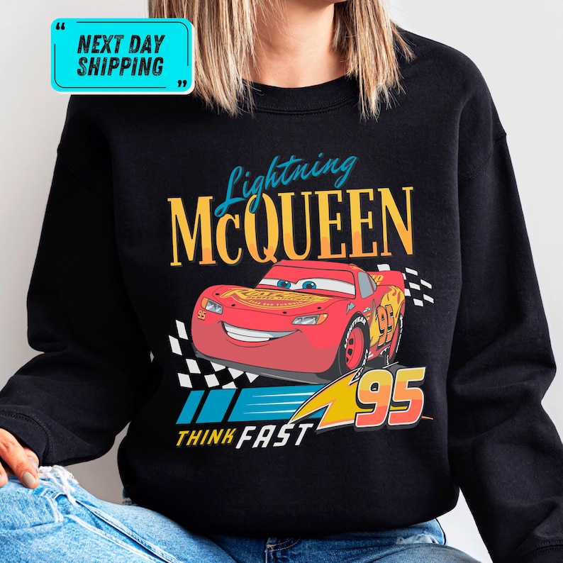 A person wearing a black sweatshirt with a graphic design featuring a red car and the text "Lightning McQueen" and "95" printed on it.