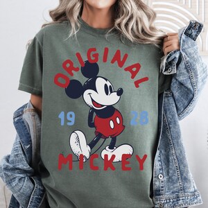 A woman wearing a green t-shirt with a graphic of Mickey Mouse and the text "ORIGINAL MICKEY" printed on it.