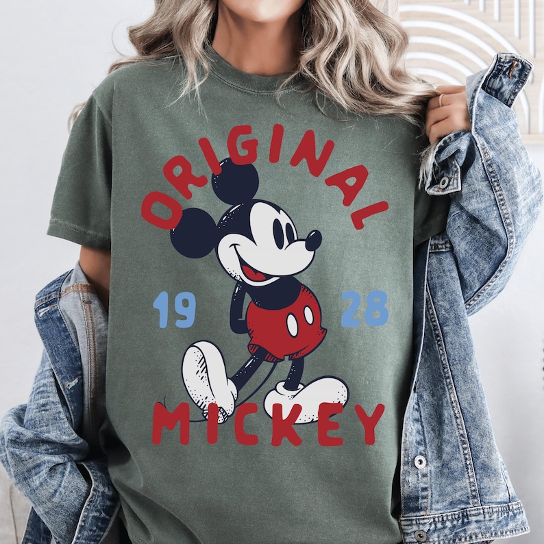 A woman wearing a green t-shirt with a graphic of Mickey Mouse and the text "ORIGINAL MICKEY" printed on it.
