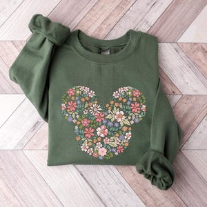 May include: A green sweatshirt featuring a floral Mickey Mouse design. The flowers are in shades of pink, yellow, and green.