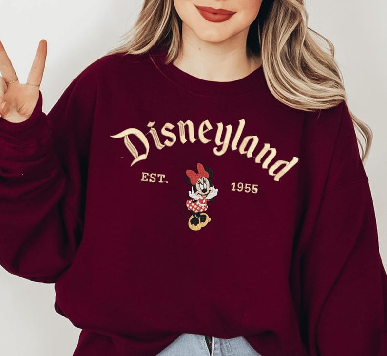 A woman wearing a burgundy sweater with the text "Disneyland EST. 1955" and a Minnie Mouse graphic.