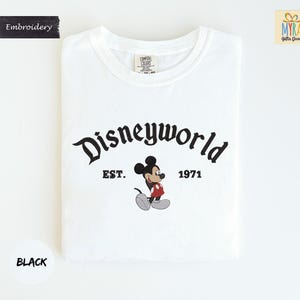 A white t-shirt with the text "Disneyworld" and "EST. 1971" printed on it, along with a Mickey Mouse graphic.