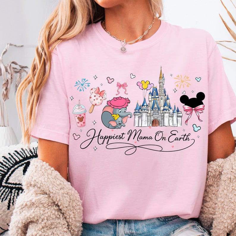 A woman wearing a pink t-shirt with a Disney-themed design, including a castle, Mickey Mouse, and other Disney characters.