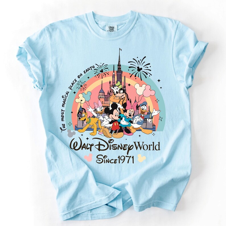 A light blue t-shirt with a Disney-themed graphic design featuring Mickey Mouse, Minnie Mouse, Donald Duck, and other Disney characters. The text on the t-shirt reads "The most magical place on earth" and "Walt Disney World Since 1971".