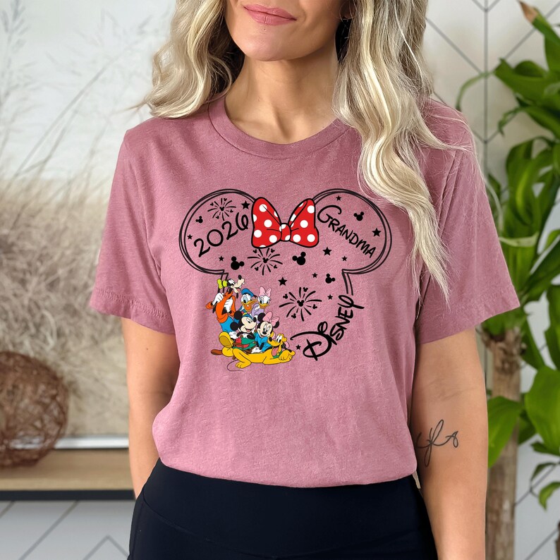 A woman wearing a pink t-shirt with a Disney-themed design, including Minnie Mouse and Mickey Mouse characters, along with the text "2020 Grandma" and "Disney".