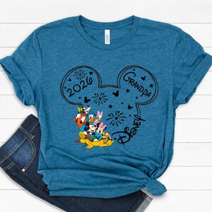 A blue t-shirt with a graphic design featuring Disney characters and the text "2020 Grandpa Disney" printed on it.