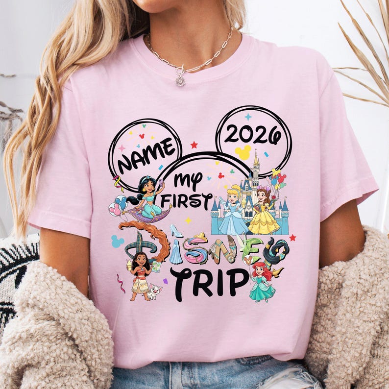 A woman wearing a pink t-shirt with a Disney-themed design, including characters from the Disney film series and the text "Name my first Disney trip".