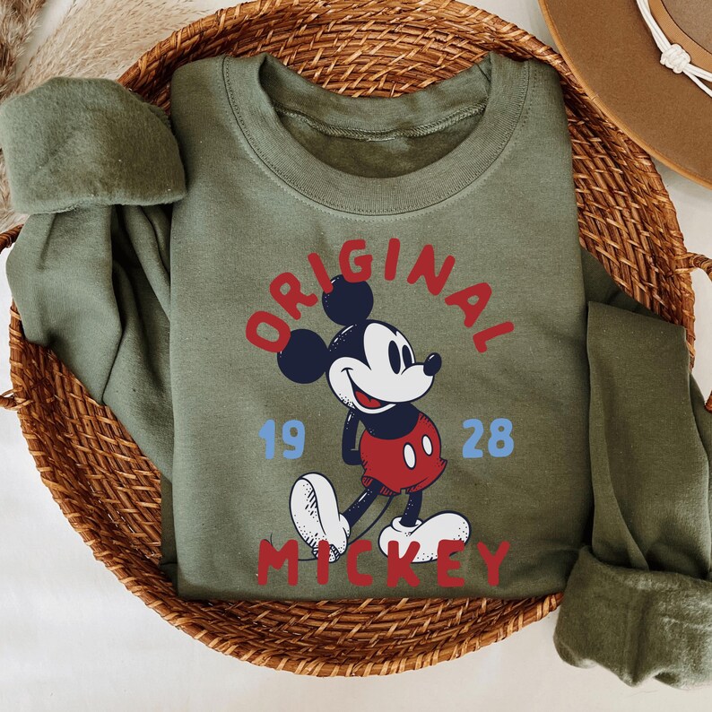 A green t-shirt with a Mickey Mouse graphic and the text "ORIGINAL" and "MILKEY" printed on it, placed in a woven basket.