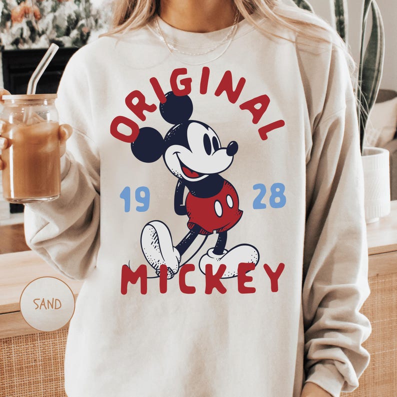 A person wearing a white sweatshirt with a graphic of Mickey Mouse and the text "ORIGINAL MICKEY" printed on it.