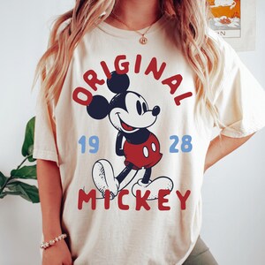 A woman wearing a white t-shirt with a graphic of Mickey Mouse and the text "ORIGINAL MICKEY" printed on it.