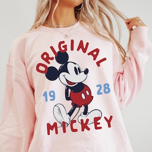 A woman wearing a pink sweatshirt with a graphic of Mickey Mouse printed on it.