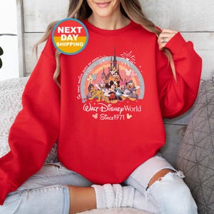 May include: Red sweatshirt with a colorful graphic of Mickey Mouse and friends at Walt Disney World. The text reads "The most magical place on Earth" and "Walt Disney World Since 1971".