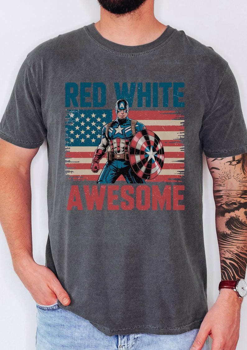 A person wearing a gray t-shirt with a graphic design featuring a superhero character and the text "RED WHITE AWESOME" printed on it.