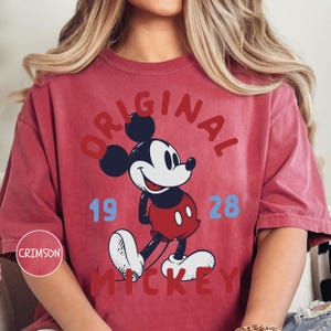 A person wearing a red t-shirt with a graphic of Mickey Mouse and the text "ORIGINAL MICKEY" printed on it.