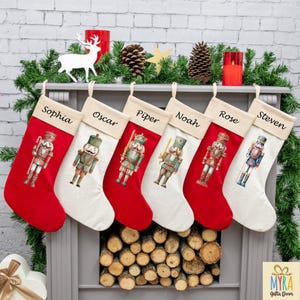 May include: Six Christmas stockings, each with a name: Sophia, Oscar, Piper, Noah, Rose, and Steven. The stockings have a red base and a white top, each with a nutcracker design. They are displayed on a mantelpiece decorated with festive greenery and candles.