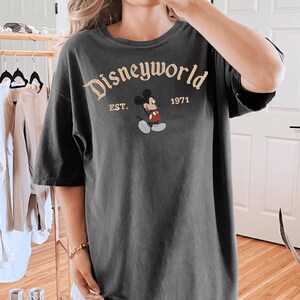 A person wearing a black t-shirt with the text "Disneyworld EST. 1971" printed on it, along with a Mickey Mouse graphic.