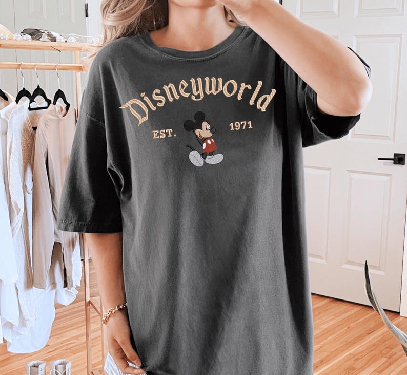 A person wearing a black t-shirt with the text "Disneyworld EST. 1971" printed on it, along with a Mickey Mouse graphic.