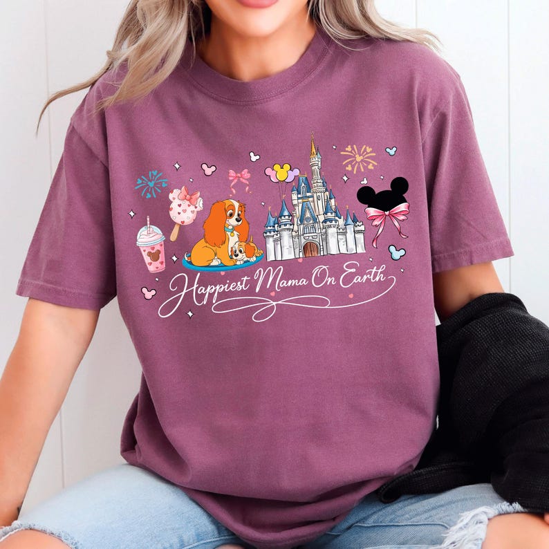 A woman wearing a purple t-shirt with a Disney-themed design, including a castle, a dog, and various Disney characters.