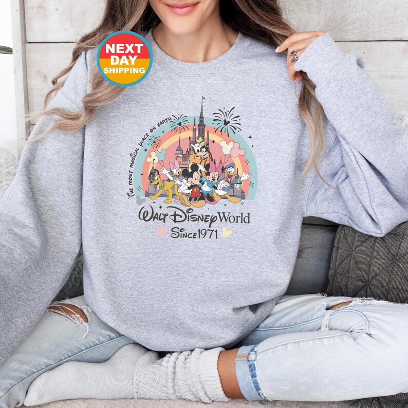 May include: A gray sweatshirt with a colorful graphic of Mickey Mouse and friends in front of Cinderella's Castle. The text "The most magical place on Earth" and "Walt Disney World Since 1971" are printed on the sweatshirt.