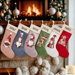May include: Six Christmas stockings in different colours, each personalised with a name in black. The stockings are decorated with festive designs including gnomes, a reindeer, and a Christmas tree. They are displayed in front of a fireplace.