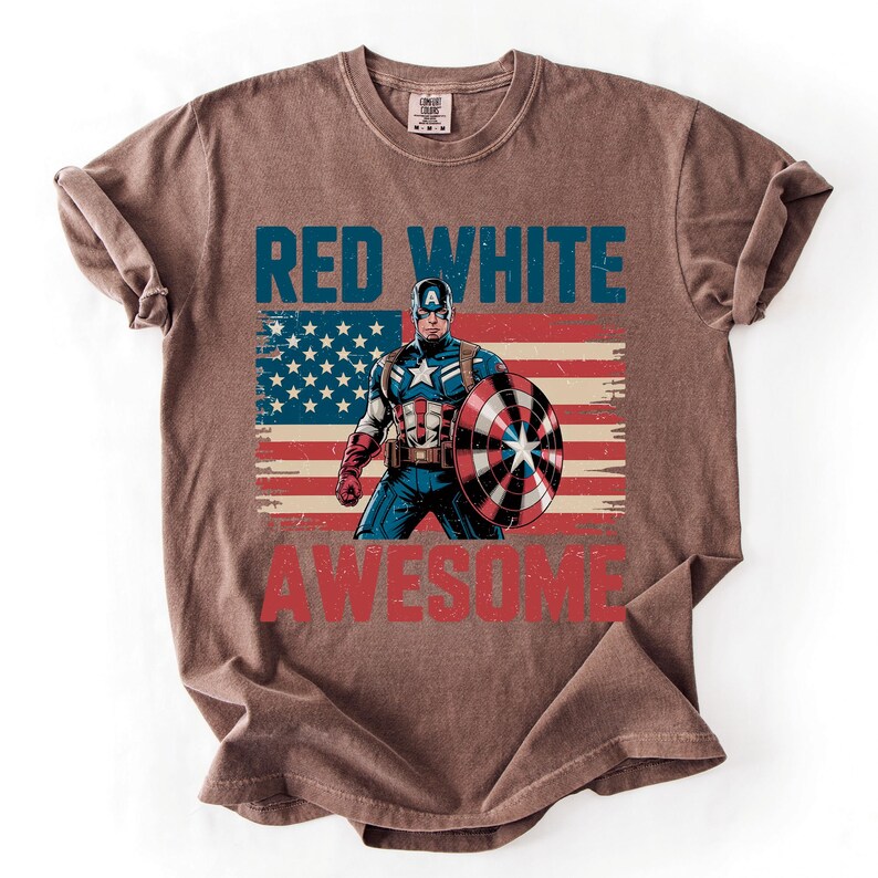 A t-shirt with a graphic design featuring a superhero character, specifically Captain America, holding a shield and standing in front of an American flag. The text on the t-shirt reads "RED WHITE AWESOME".