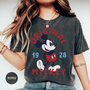 A woman wearing a gray t-shirt with a graphic of Mickey Mouse and the text "ORIGINAL MICKEY" printed on it.