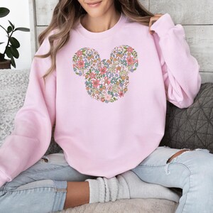 May include: A pink sweatshirt featuring a floral Mickey Mouse design. The flowers are in shades of pink, yellow and blue.