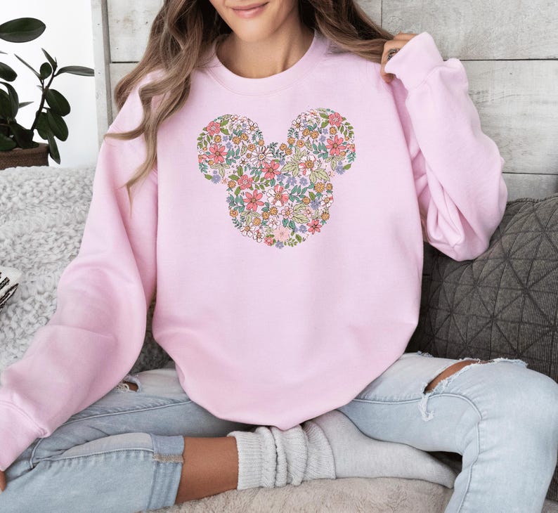 May include: A pink sweatshirt featuring a floral Mickey Mouse design. The flowers are in shades of pink, yellow and blue.