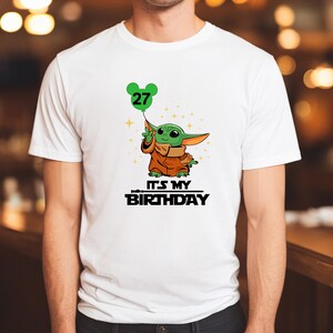 A white t-shirt with a graphic design featuring a cartoon character holding a balloon with the number 27 on it, along with the text "It's MY BIRTHDAY".