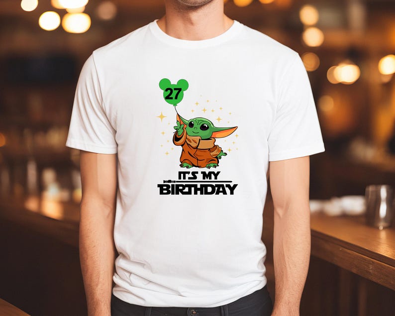 A white t-shirt with a graphic design featuring a cartoon character holding a balloon with the number 27 on it, along with the text "It's MY BIRTHDAY".