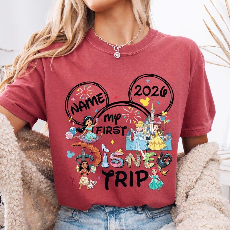 A person wearing a red t-shirt with Disney-themed graphics and text, including the words "Name my first Disney trip" and "2020".