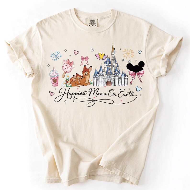 A white t-shirt with a printed design featuring Disney characters and landmarks, along with the text "Happiest Mama On Earth".