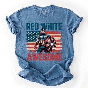 A blue t-shirt with a graphic design featuring a superhero character and the text "RED WHITE AWESOME" printed on it.