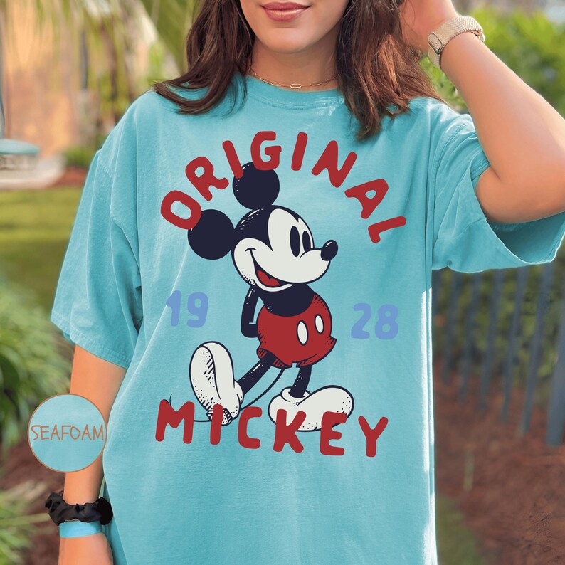 A woman wearing a blue t-shirt with a Mickey Mouse graphic and the text "ORIGINAL MICKEY" printed on it.