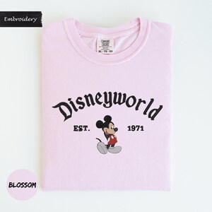 A pink t-shirt with the text "Disneyworld" and a Mickey Mouse graphic, along with the text "EST. 1971" and "BLOSSOM" printed on it.