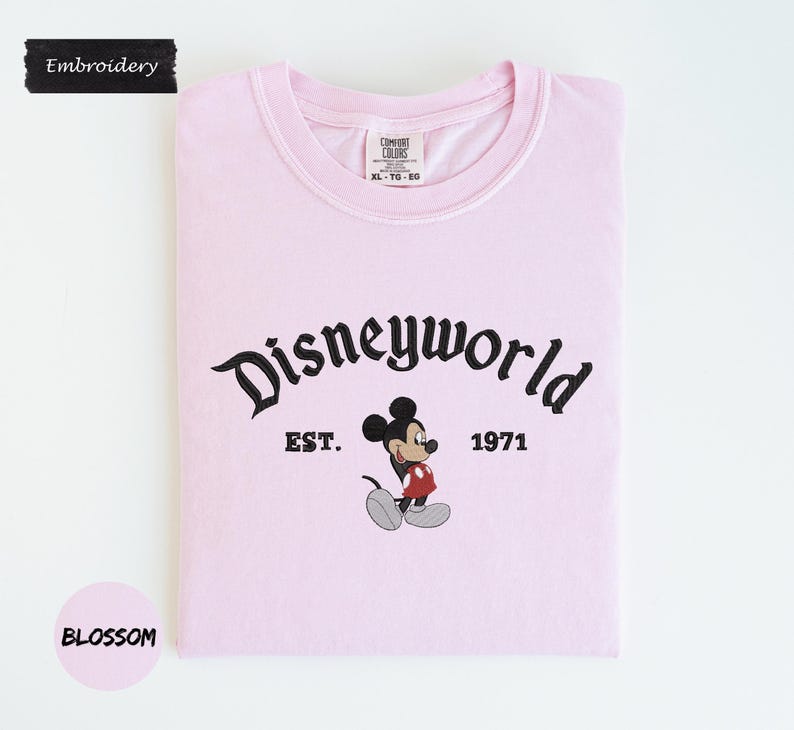 A pink t-shirt with the text "Disneyworld" and a Mickey Mouse graphic, along with the text "EST. 1971" and "BLOSSOM" printed on it.