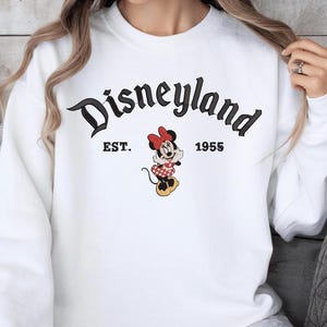A white sweatshirt with the text "Disneyland EST. 1955" and an image of Minnie Mouse, a character from the Disney theme park.